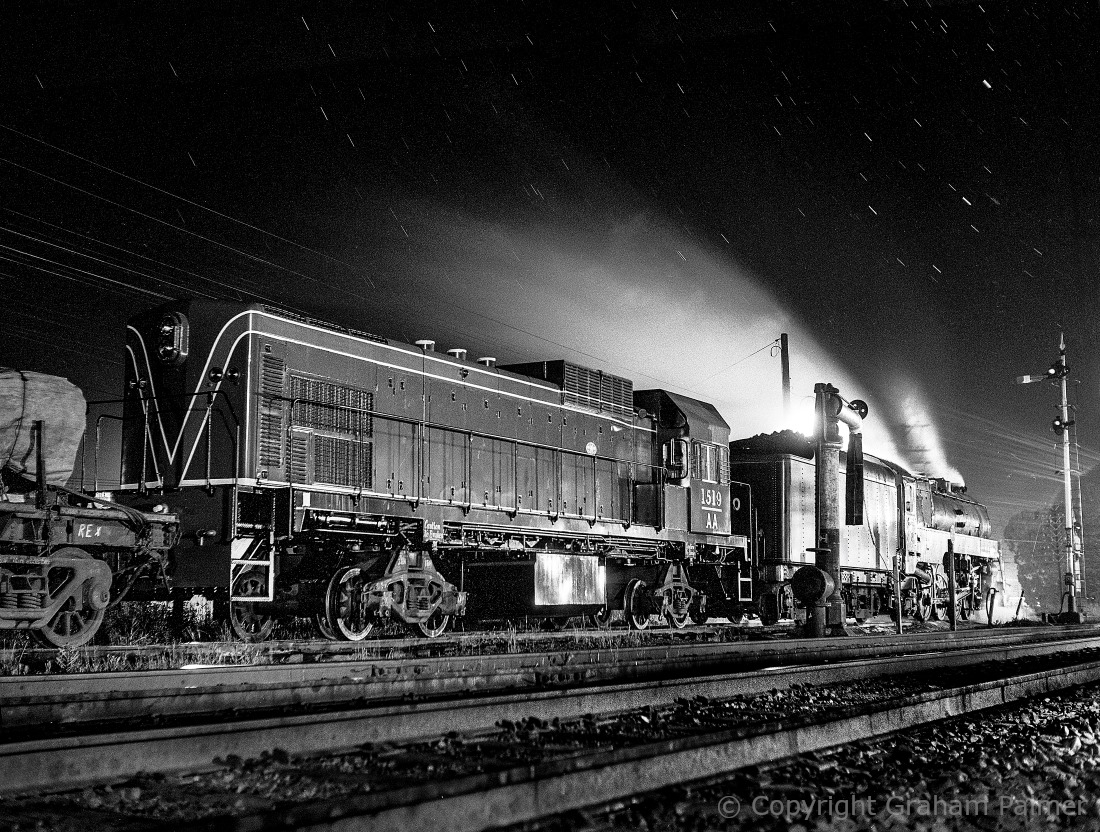 A night photograph of West Australian AA class diesel 1519 being hauled past Bargo by steam locomotive 3830 in the rain, 1967.