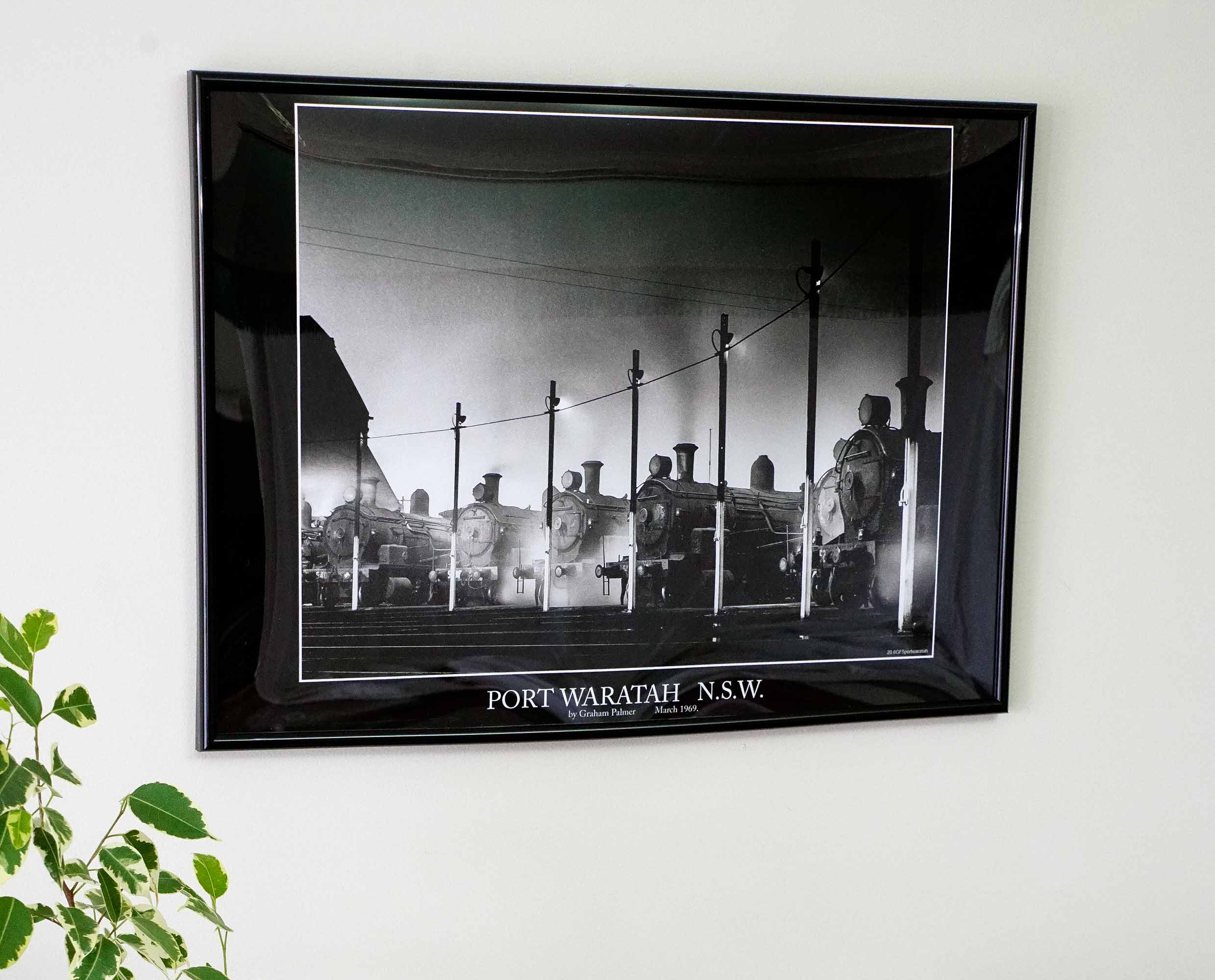 A framed black-and-white print of steam locomotives at Port Waratah displayed on a wall.